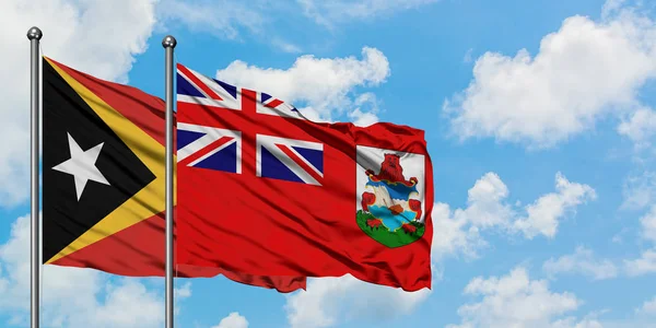 Timor Oriental y la bandera de las Bermudas ondeando en el viento contra el cielo azul nublado blanco juntos. Concepto diplomático, relaciones internacionales . — Foto de Stock