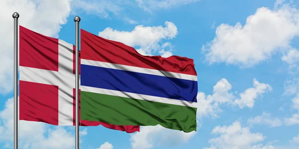 Danimarca e Gambia sventolano nel vento contro il cielo bianco nuvoloso blu insieme. Concetto di diplomazia, relazioni internazionali . — Foto Stock