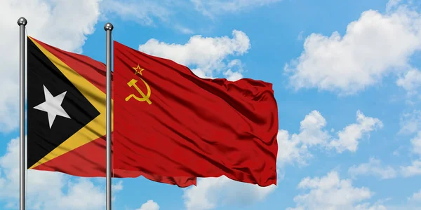 Timor Oriental y la bandera de la Unión Soviética ondeando en el viento contra el cielo azul nublado blanco juntos. Concepto diplomático, relaciones internacionales . —  Fotos de Stock
