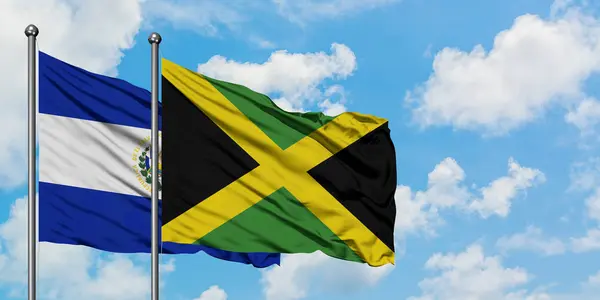 Bandera de El Salvador y Jamaica ondeando en el viento contra el cielo azul nublado blanco juntos. Concepto diplomático, relaciones internacionales . — Foto de Stock