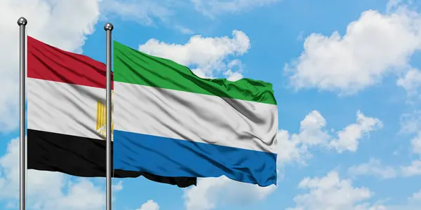 Bandera de Egipto y Sierra Leona ondeando en el viento contra el cielo azul nublado blanco juntos. Concepto diplomático, relaciones internacionales . — Foto de Stock