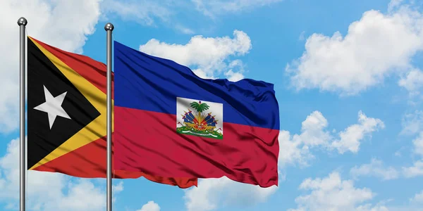 Timor Oriental y la bandera de Haití ondeando en el viento contra el cielo azul nublado blanco juntos. Concepto diplomático, relaciones internacionales . — Foto de Stock