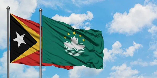 Timor Oriental y la bandera de Macao ondeando en el viento contra el cielo azul nublado blanco juntos. Concepto diplomático, relaciones internacionales . — Foto de Stock
