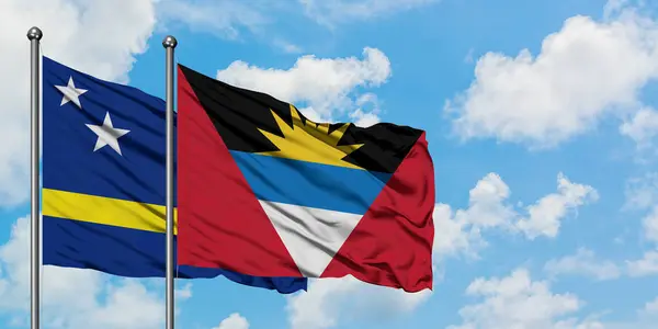 Curacao ve Antigua ve Barbuda bayrağı birlikte beyaz bulutlu mavi gökyüzüne karşı rüzgarda sallayarak. Diplomasi kavramı, uluslararası ilişkiler. — Stok fotoğraf