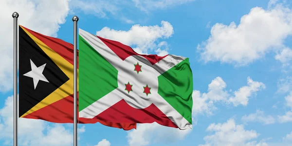 Timor Oriental y la bandera de Burundi ondeando en el viento contra el cielo azul nublado blanco juntos. Concepto diplomático, relaciones internacionales . — Foto de Stock