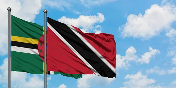 Bandera de Dominica y Trinidad y Tobago ondeando en el viento contra el cielo azul nublado blanco juntos. Concepto diplomático, relaciones internacionales . — Foto de Stock