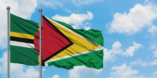 Bandera de Dominica y Guyana ondeando en el viento contra el cielo azul nublado blanco juntos. Concepto diplomático, relaciones internacionales . — Foto de Stock