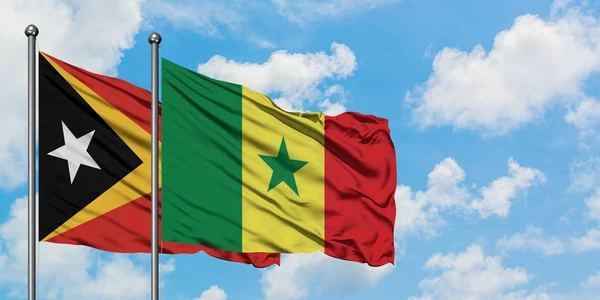 Timor Oriental y la bandera de Senegal ondeando en el viento contra el cielo azul nublado blanco juntos. Concepto diplomático, relaciones internacionales . — Foto de Stock