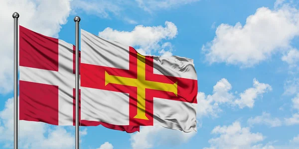 Danmark och Guernsey flagga vifta i vinden mot vit grumlig blå himmel tillsammans. Diplomatisk koncept, internationella relationer. — Stockfoto