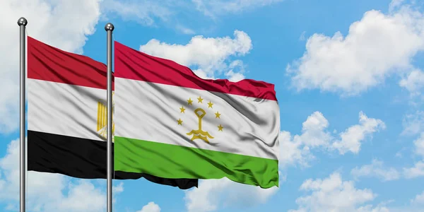 Bandera de Egipto y Tayikistán ondeando en el viento contra el cielo azul nublado blanco juntos. Concepto diplomático, relaciones internacionales . — Foto de Stock