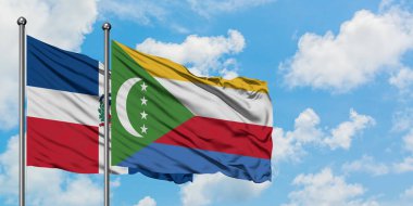 Dominik Cumhuriyeti ve Komor bayrağı birlikte beyaz bulutlu mavi gökyüzüne karşı rüzgarda sallayarak. Diplomasi kavramı, uluslararası ilişkiler.