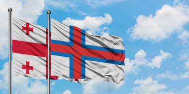 Gürcistan ve Faroe Adaları bayrağı birlikte beyaz bulutlu mavi gökyüzüne karşı rüzgarda sallayarak. Diplomasi kavramı, uluslararası ilişkiler.