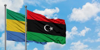 Gabon ve Libya bayrağı birlikte beyaz bulutlu mavi gökyüzüne karşı rüzgarda sallayarak. Diplomasi kavramı, uluslararası ilişkiler.