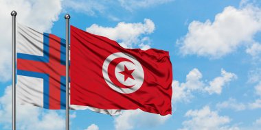 Faroe Adaları ve Tunus bayrağı birlikte beyaz bulutlu mavi gökyüzüne karşı rüzgarda sallayarak. Diplomasi kavramı, uluslararası ilişkiler.