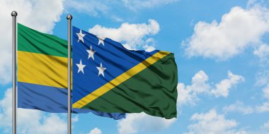 Gabon ve Solomon Adaları bayrağı birlikte beyaz bulutlu mavi gökyüzüne karşı rüzgarda sallayarak. Diplomasi kavramı, uluslararası ilişkiler.
