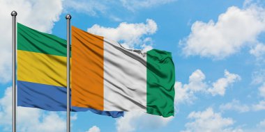 Gabon ve Fildişi Sahili bayrağı birlikte beyaz bulutlu mavi gökyüzüne karşı rüzgarda sallayarak. Diplomasi kavramı, uluslararası ilişkiler.