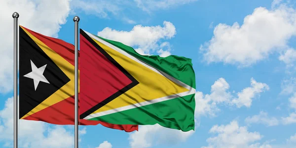 Timor Oriental y Guyana bandera ondeando en el viento contra el cielo azul nublado blanco juntos. Concepto diplomático, relaciones internacionales . — Foto de Stock
