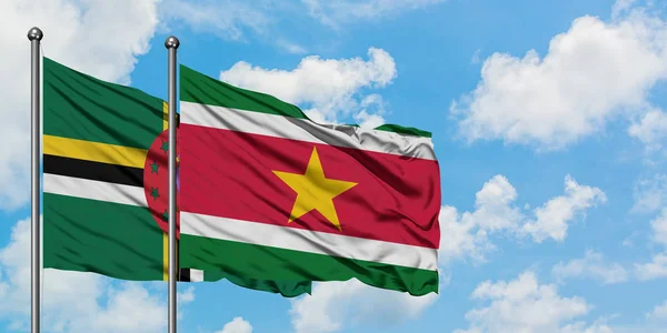 Drapeau de la Dominique et du Suriname agitant dans le vent contre ciel bleu nuageux blanc ensemble. Concept de diplomatie, relations internationales . — Photo