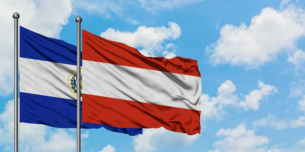 Bandera de El Salvador y Austria ondeando en el viento contra el cielo azul nublado blanco juntos. Concepto diplomático, relaciones internacionales . — Foto de Stock