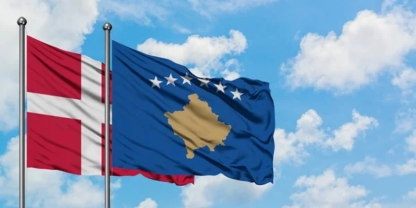 A bandeira da Dinamarca e do Kosovo agitando no vento contra o céu azul nublado branco juntos. Conceito de diplomacia, relações internacionais . — Fotografia de Stock