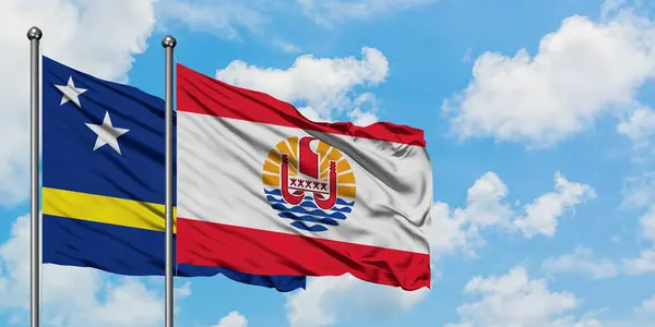 Curazao y la bandera de la Polinesia Francesa ondeando en el viento contra el cielo azul nublado blanco juntos. Concepto diplomático, relaciones internacionales . — Foto de Stock