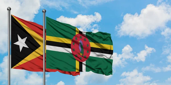 Timor Oriental y la bandera de Dominica ondeando en el viento contra el cielo azul nublado blanco juntos. Concepto diplomático, relaciones internacionales . — Foto de Stock