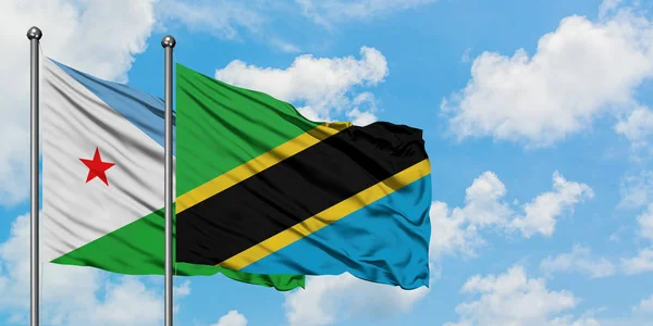 Djibouti a tanzanská vlajka mávali ve větru proti bílé oblačné obloze. Diplomacie, mezinárodní vztahy. — Stock fotografie