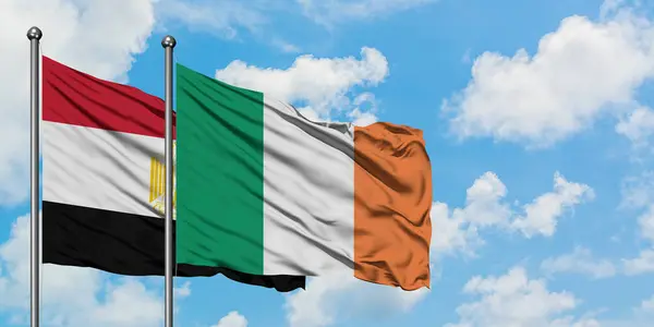 Bandera de Egipto e Irlanda ondeando en el viento contra el cielo azul nublado blanco juntos. Concepto diplomático, relaciones internacionales . — Foto de Stock