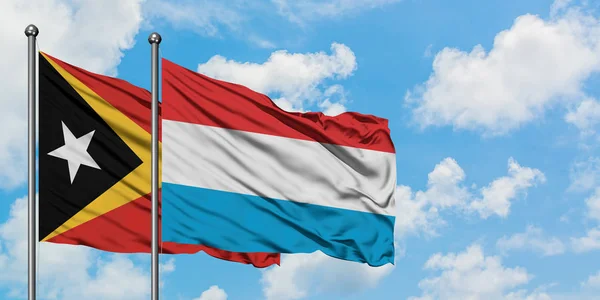Timor Oriental y la bandera de Luxemburgo ondeando en el viento contra el cielo azul nublado blanco juntos. Concepto diplomático, relaciones internacionales . — Foto de Stock