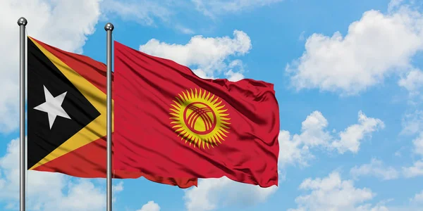 Timor Oriental y la bandera de Kirguistán ondeando en el viento contra el cielo azul nublado blanco juntos. Concepto diplomático, relaciones internacionales . — Foto de Stock