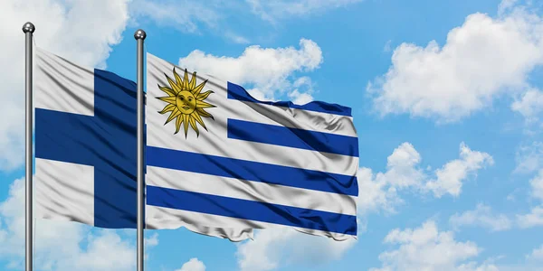 Bandera de Finlandia y Uruguay ondeando en el viento contra el cielo azul nublado blanco juntos. Concepto diplomático, relaciones internacionales . —  Fotos de Stock