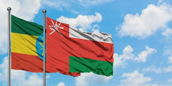 Bandera de Etiopía y Omán ondeando en el viento contra el cielo azul nublado blanco juntos. Concepto diplomático, relaciones internacionales . — Foto de Stock