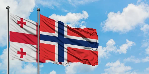 Bandera de Georgia y Bouvet Islands ondeando en el viento contra el cielo azul nublado blanco juntos. Concepto diplomático, relaciones internacionales . — Foto de Stock