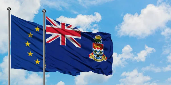 Bandera de la Unión Europea y las Islas Caimán ondeando en el viento contra el cielo azul nublado blanco juntos. Concepto diplomático, relaciones internacionales . — Foto de Stock