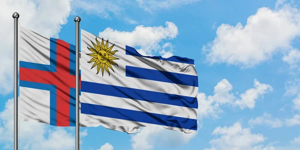 Bandera de las Islas Feroe y Uruguay ondeando en el viento contra el cielo azul nublado blanco juntos. Concepto diplomático, relaciones internacionales . —  Fotos de Stock