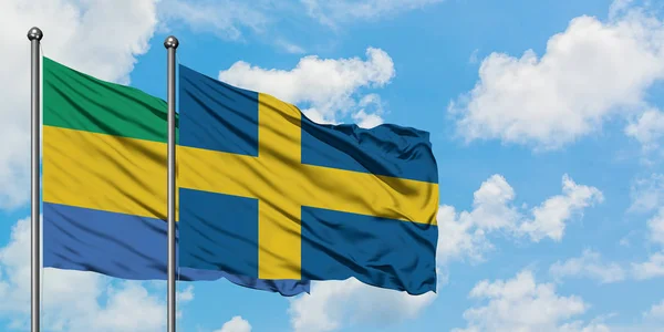 Флаг Габона и Швеции размахивает ветром против белого облачно-голубого неба вместе. Концепция дипломатии, международные отношения . — стоковое фото