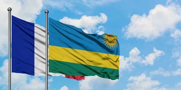 Bandera de Francia y Ruanda ondeando en el viento contra el cielo azul nublado blanco juntos. Concepto diplomático, relaciones internacionales . — Foto de Stock