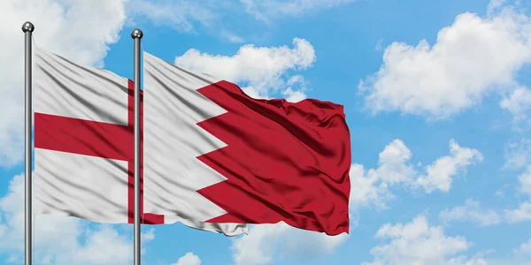 Anglie a Bahrašin vlaje ve větru proti bíle zatažené modré obloze. Diplomacie, mezinárodní vztahy. — Stock fotografie