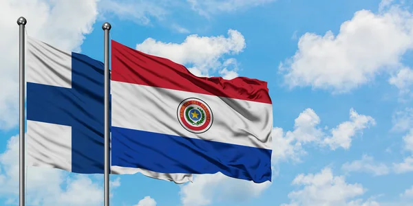 Bandera de Finlandia y Paraguay ondeando en el viento contra el cielo azul nublado blanco juntos. Concepto diplomático, relaciones internacionales . — Foto de Stock