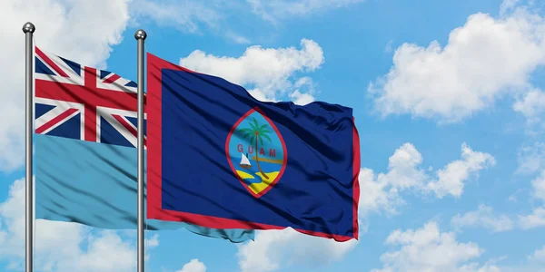 Bandera de Fiyi y Guam ondeando en el viento contra el cielo azul nublado blanco juntos. Concepto diplomático, relaciones internacionales . — Foto de Stock