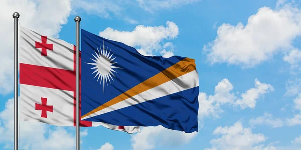 Bandera de Georgia y las Islas Marshall ondeando en el viento contra el cielo azul nublado blanco juntos. Concepto diplomático, relaciones internacionales . — Foto de Stock