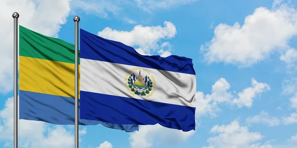 Gabon und El Salvador-Fahne wehen gemeinsam im Wind gegen den wolkenverhangenen blauen Himmel. Diplomatie-Konzept, internationale Beziehungen. — Stockfoto