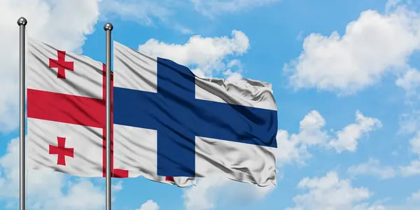 Georgia a Finsko vlají ve větru proti bíle zatažené modré obloze. Diplomacie, mezinárodní vztahy. — Stock fotografie