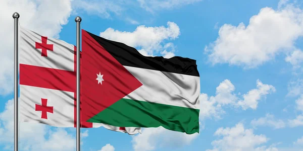 Bandera de Georgia y Jordania ondeando en el viento contra el cielo azul nublado blanco juntos. Concepto diplomático, relaciones internacionales . — Foto de Stock