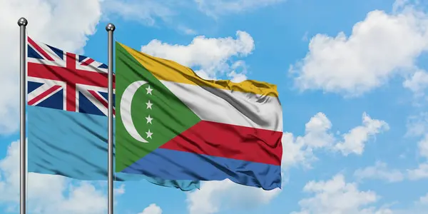 Bandera de Fiyi y Comoras ondeando en el viento contra el cielo azul nublado blanco juntos. Concepto diplomático, relaciones internacionales . — Foto de Stock