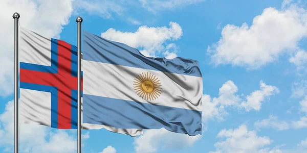 Bandera de las Islas Feroe y Argentina ondeando en el viento contra el cielo azul nublado blanco juntos. Concepto diplomático, relaciones internacionales . — Foto de Stock