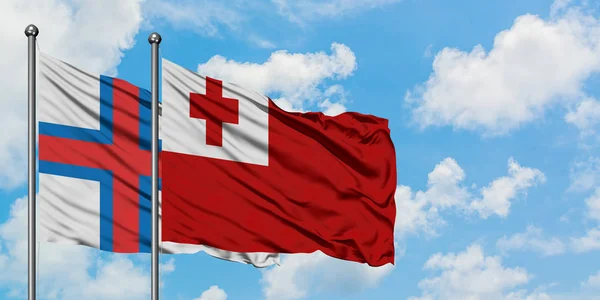 Ilhas Faroé e bandeira Tonga acenando no vento contra o céu azul nublado branco juntos. Conceito de diplomacia, relações internacionais . — Fotografia de Stock