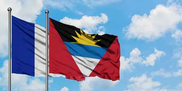 Fransa ve Antigua ve Barbuda bayrağı birlikte beyaz bulutlu mavi gökyüzüne karşı rüzgarda sallayarak. Diplomasi kavramı, uluslararası ilişkiler. — Stok fotoğraf