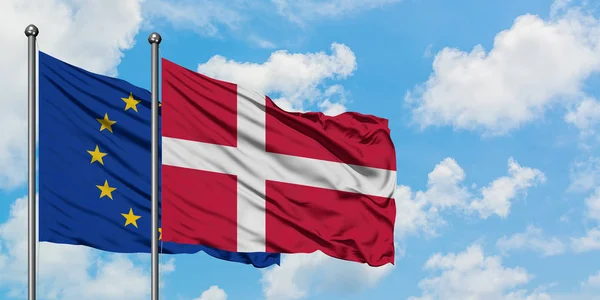 Vlajka Evropské unie a Dánska vlaje ve větru proti bíle zatažené modré obloze. Diplomacie, mezinárodní vztahy. — Stock fotografie