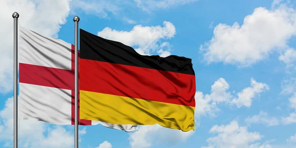 England- und Deutschland-Flagge wehen gemeinsam im Wind vor dem weiß-wolkenverhangenen blauen Himmel. Diplomatie-Konzept, internationale Beziehungen. — Stockfoto